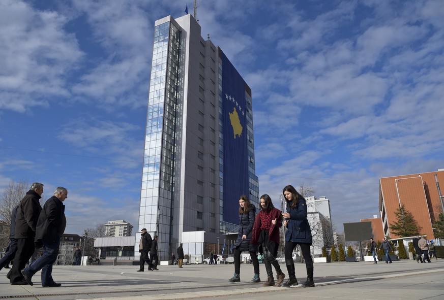 People walk past the government building decorated with a giant Kosovo national flag placed for the upcoming 10th independence anniversary, in Pristina on Friday, Feb. 9, 2018. Kosovo declared indepen ...
