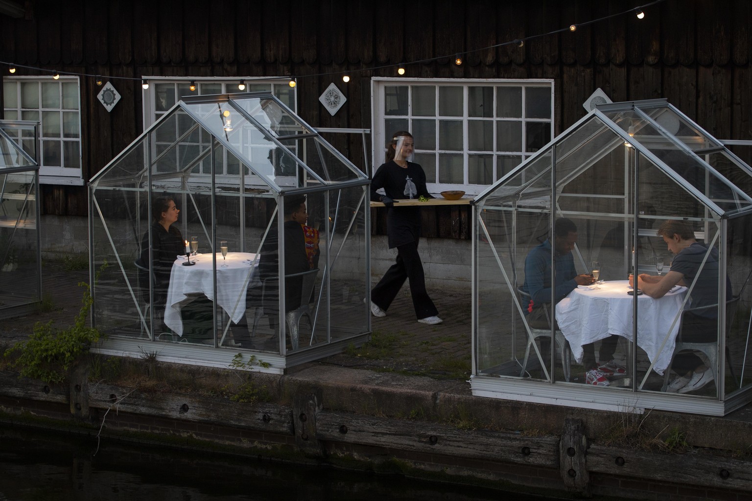FILE - In this May 5, 2020 file photo, staff at the Mediamatic restaurant serve food to volunteers seated in small glasshouses during a try-out of a setup which respects social distancing abiding by g ...