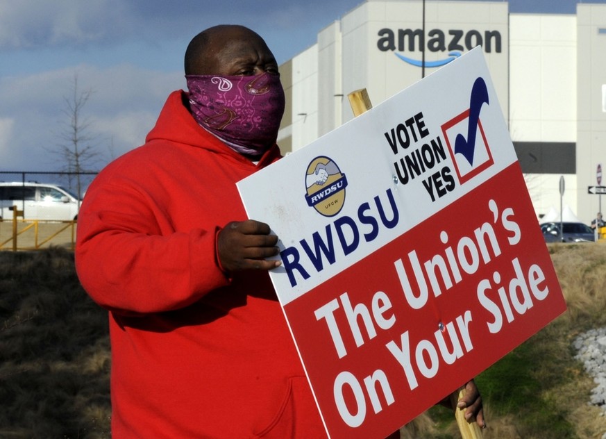 FILE - In this Tuesday, Feb. 9, 2021 file photo ,Michael Foster of the Retail, Wholesale and Department Store Union holds a sign outside an Amazon facility where labor is trying to organize workers in ...