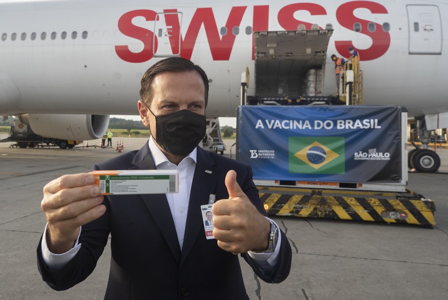 Sao Paulo Gov. Joao Doria poses for photo flashing a thumbs up next to a container carrying the experimental COVID-19 vaccine CoronaVac after it was unloaded from a cargo plane that arrived from China ...