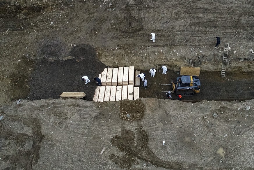 Workers wearing personal protective equipment bury bodies in a trench on Hart Island, Thursday, April 9, 2020, in the Bronx borough of New York. New York City Mayor Bill DeBlasio said earlier in the w ...