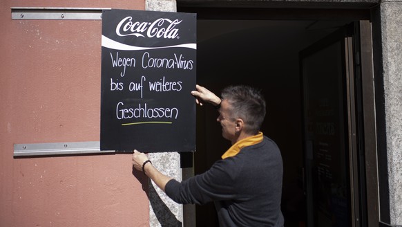 epa08298699 Linus Caduff hangs a sign in front of the Cafe Arcas with the inscription &#039;Closed for coronavirus until further notice&#039;, in Chur, Switzerland, 16 March 2020. The local government ...