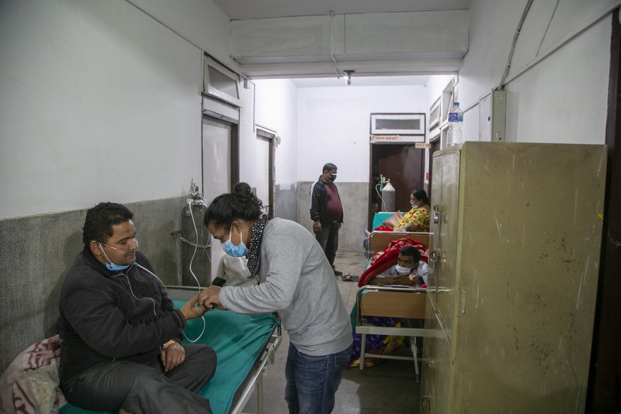 A family member gives medicine to a COVID-19 patient on the corridor of the emergency ward of a hospital in Kathmandu, Nepal, Wednesday, May 5, 2021. Authorities extended lockdown in the capital Kathm ...