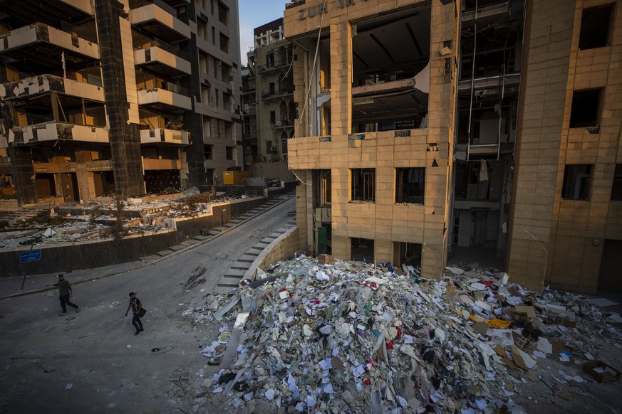 People walk next debris from destroyed buildings near the site of last week&#039;s explosion that hit the seaport of Beirut, Lebanon, Wednesday, Aug. 12, 2020. (AP Photo/Hassan Ammar)