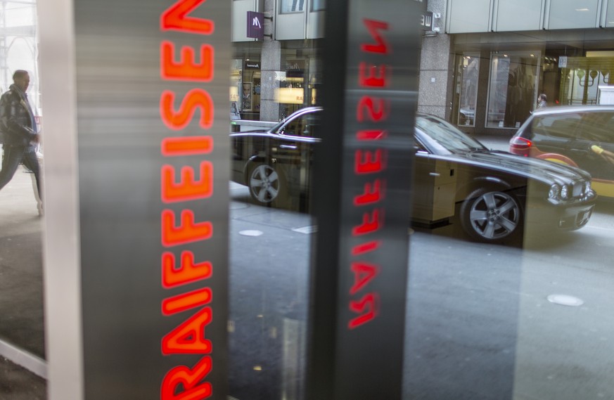 ARCHIV - Das Firmenlogo der Bank Raiffeisen in Zug, im Hintergrund steht ein Jaguar auf der Bahnhofstrasse, aufgenommen am 22. Februar 2013. Die Schweizerische Nationalbank (SNB) stuft die Raiffeisen  ...