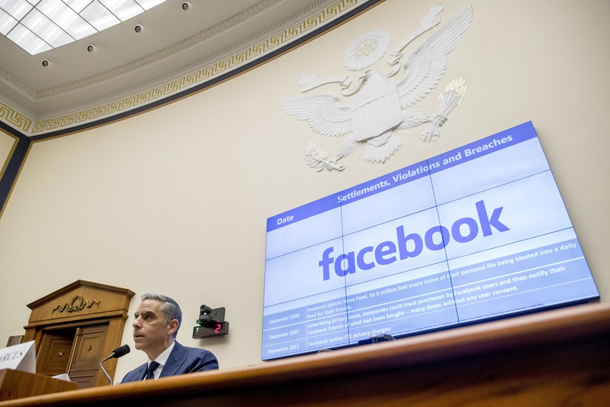 A list of settlements, violations and breaches scrolls over Facebook&#039;s logo on a screen behind David Marcus, CEO of Facebook&#039;s Calibra digital wallet service, left, as he speaks during a Hou ...