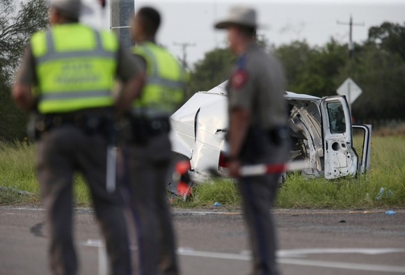 Texas Department of Public Safety officers stand near a vehicle where multiple people died after the van carrying migrants tipped over just south of the Brooks County community of Encino on Wednesday, ...