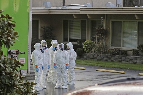 Workers from a Servpro disaster recovery team wearing protective suits and respirators wait before entering the Life Care Center in Kirkland, Wash. to begin cleaning and disinfecting the facility, Wed ...