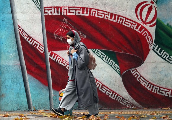 epa08859346 An Iranian girl walks past a mural with Iran&#039;s national flag in a street in Tehran, Iran, 03 December 2020. Iranian president Rouhani said that his government does not agree with the  ...