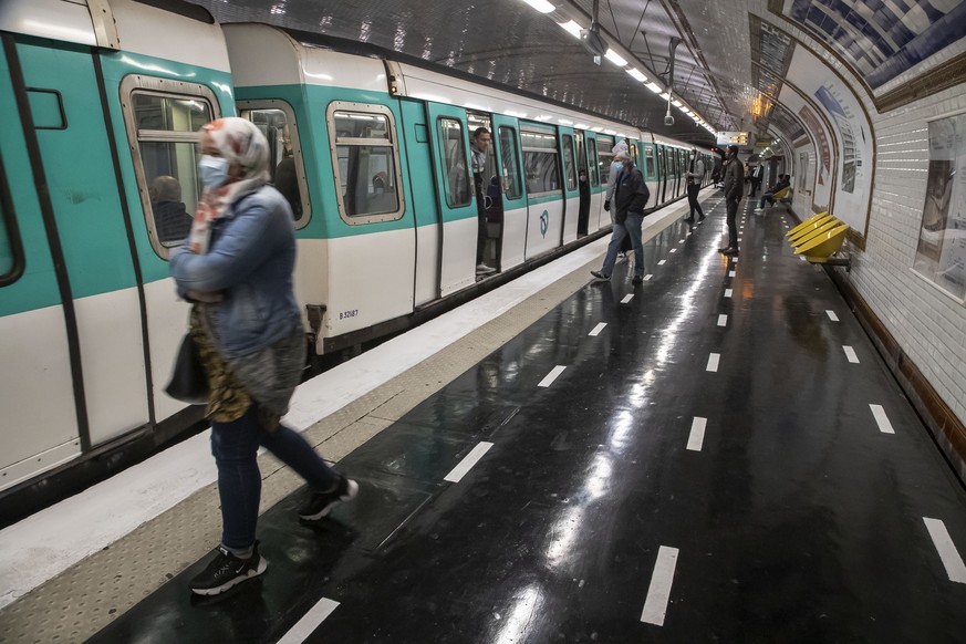 People with mask walk over marks on the ground meant to encourage social distancing to protect against the spread of the coronavirus as they board a subway in Paris, Tuesday, May 5, 2020. France prepa ...