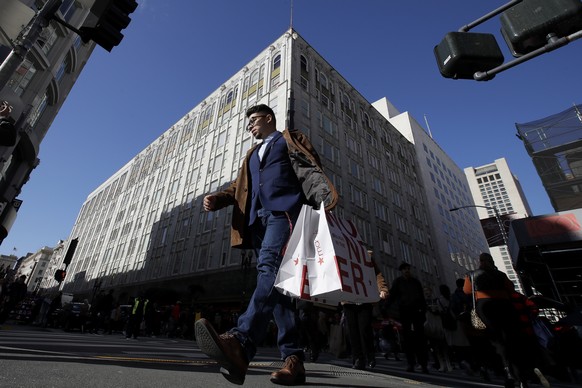FILE - In this Nov. 29, 2019, file photo, man carries shopping bags across the street from a Macy&#039;s store in San Francisco. Macy&#039;s says it is closing 125 of its least productive stores and c ...
