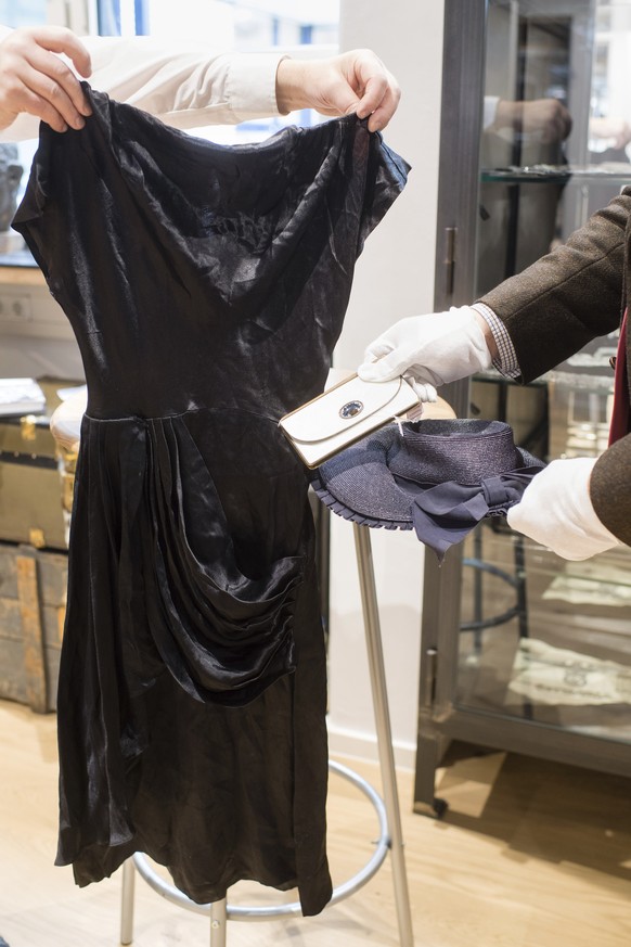 Empolyees hold a cocktail dress, a wallet and a strawhat that belonged to Eva Braun the wife of Adolf Hitler prior to an auction in Grasbrunn, Germany, Wednesday, Nov. 20, 2019. A Jewish group has sha ...