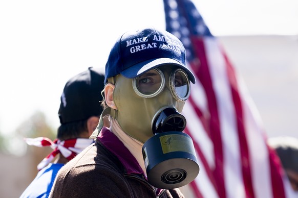 epa08718272 A supporter of US President Donald J. Trump wears a &#039;Make America Great Again&#039; hat and a gas mask while gathering with Trump supporters wishing him well outside Walter Reed Natio ...