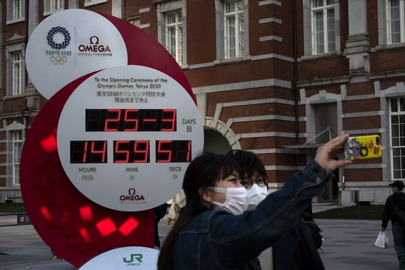 Two women take a selfie with a Tokyo 2020 countdown clock displaying the current date and time outside Tokyo Station, Wednesday, March 25, 2020, in Tokyo. Not even the Summer Olympics could withstand  ...