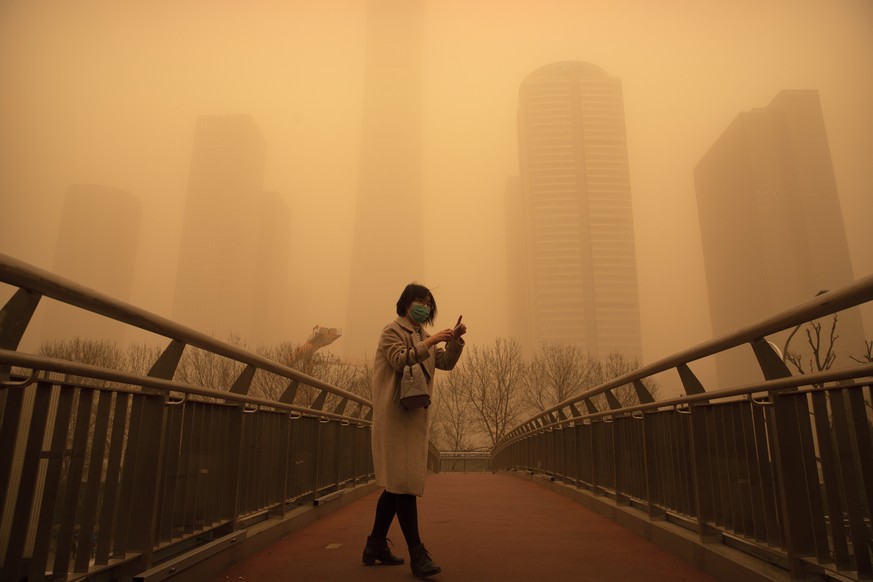 A woman walks along a pedestrian bridge amid a sandstorm during the morning rush hour in the central business district in Beijing, Monday, March 15, 2021. The sandstorm brought a tinted haze to Beijin ...
