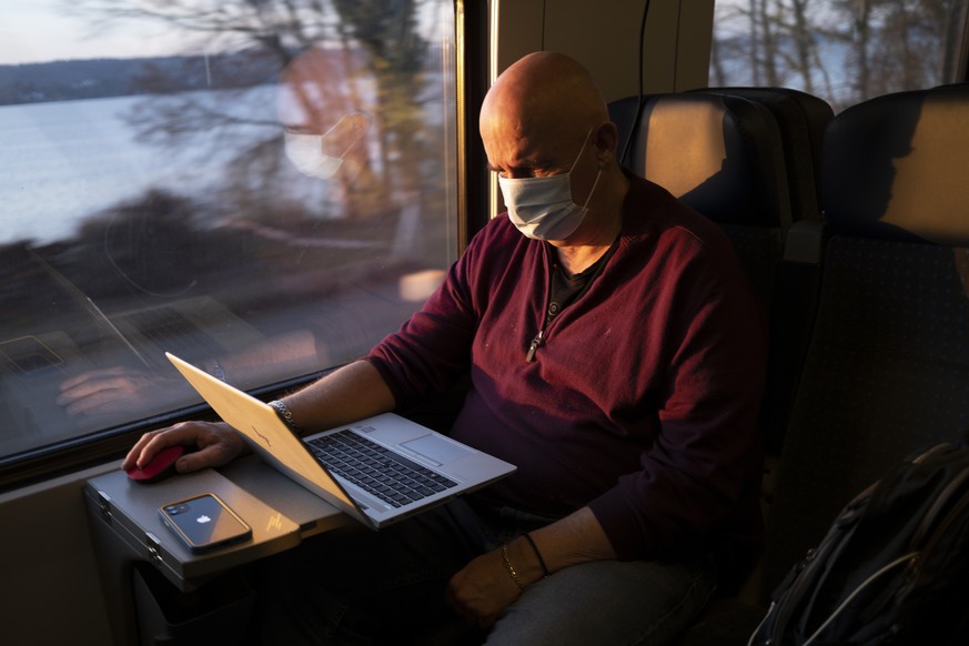 Passenger wearing protective mask works on a laptop as he rides a SBB CFF FFS train in front of the Bielersee during the coronavirus disease (COVID-19) outbreak, in Neuchatel, Switzerland, Tuesday, Ma ...