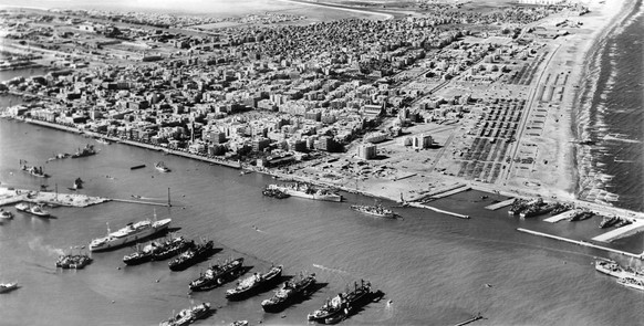 A view of the town from the east with the Port in the foreground, on 17. November 1956. The assault beaches are on the right, with some of the wooden beach huts destroyed. On the left are a dredger an ...