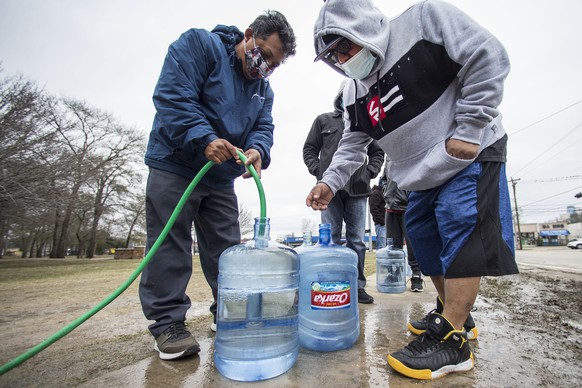 Victor Hernandez, left, and Luis Martinez fill their water containers with a hose from a spigot in Haden Park, Thursday, Feb. 18, 2021 in Houston. Texas officials have ordered 7 million people to boil ...