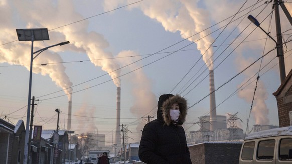 SHANXI, CHINA -NOVEMBER 26: (CHINA, HONG KONG, MACAU, TAIWAN OUT) Smoke billows from stacks as a Chinese woman wears as mask while walking in a neighborhood next to a coal fired power plant on Novembe ...