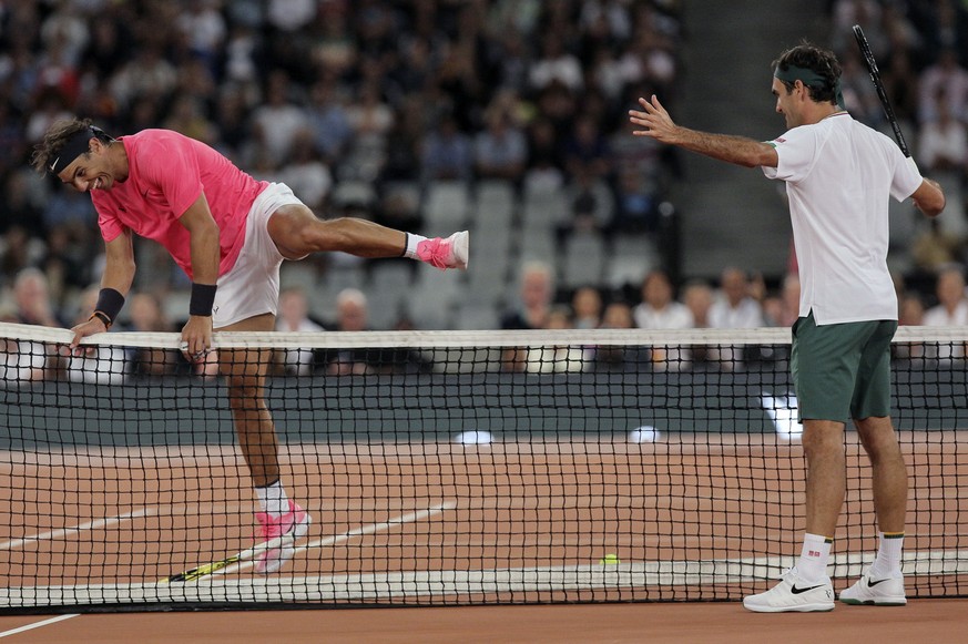 Rafael Nadal, left, jumps the net while Roger Federer watches on during their exhibition tennis match held at the Cape Town Stadium in Cape Town, South Africa, Friday Feb. 7, 2020. (AP Photo/Halden Kr ...
