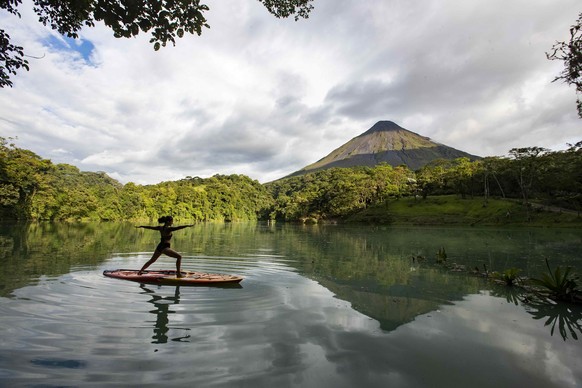 epa08640095 A woman practices yoga on a board in a lagoon from where the Arenal volcano can be seen, in La Fortuna de San Carlos area, north of San Jose, Costa Rica, 28 August 2020 (issued 01 Septembe ...