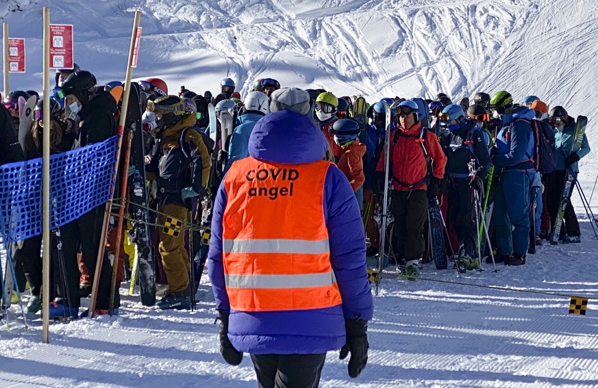 epa08941751 A ski lift staff identified as &#039;COVID Angel&#039; looks at skiers and snowboarders lining up in a queue at a ski lift during the coronavirus pandemic, in the Alpine resort of Verbier, ...