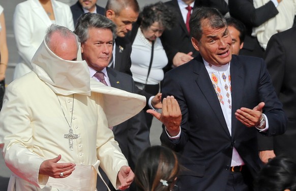 Pope Francis, left, has the mantle of his cassock whipped into his face by a gust of wind as he and Ecuador&#039;s President Rafael Correa gesture towards several children to come closer, upon the Pop ...