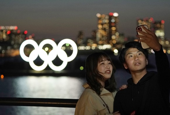 epa08321126 A couple take a selfie with giant Olympic rings monument seen in the background at dusk at Odaiba Marine Park in Tokyo, Japan, 25 March 2020. Japanese Prime Minister Shinzo Abe and Interna ...