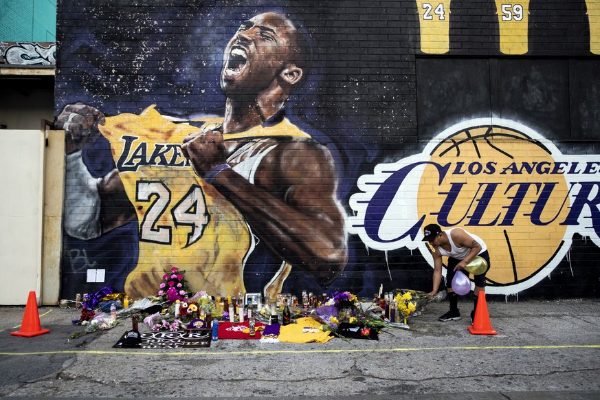 epaselect epa08171354 A man leaves flowers at a makeshift memorial in front of a mural of late Los Angeles Lakers guard Kobe Bryant near the Staples Center, home of the Los Angeles Lakers, in Los Ange ...