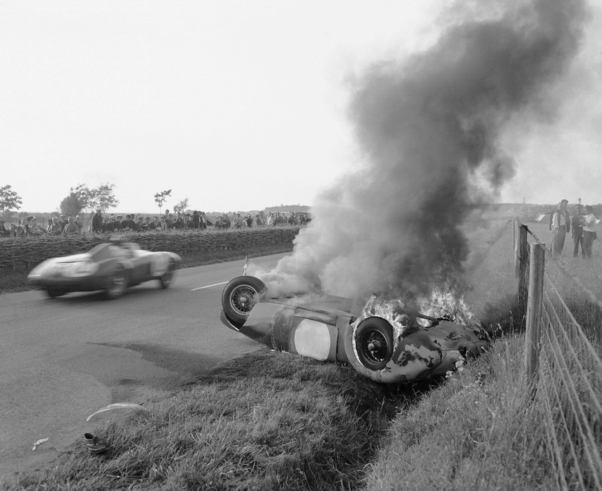 A car roars by the burning wreck of M.G. 42, driving by British R. Jacobs, which overturned in the deadly Maison Blanche bend in Le Mans, France on June 11, 1955, during the 24-hour endurance race. Ja ...