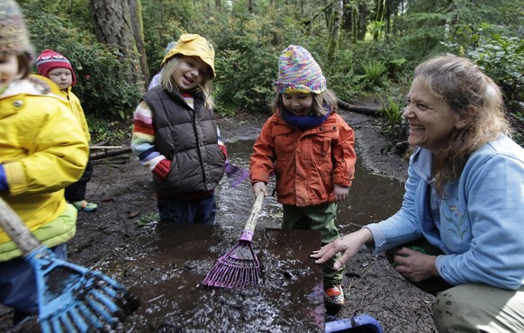 Teacher Erin Kenny, right, looks on as Lola Dammann, 4, second from left, and Beulah Ellison-Taylor, 3, second from right, explore mud spread on a table as they attend Cedarsong Nature School&#039;s o ...